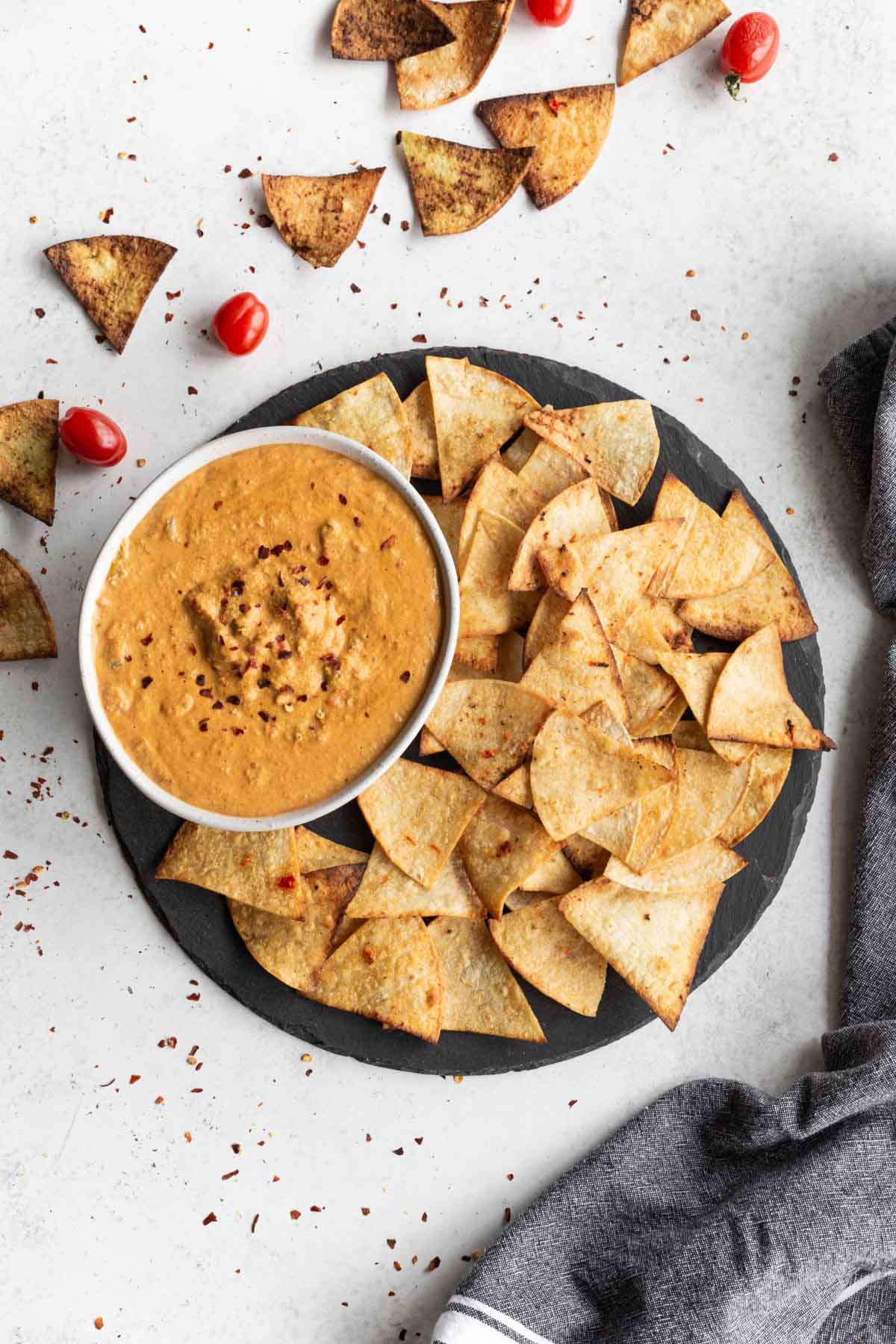 A bowl of cashew queso and tortilla chips served on a round piece of slate.