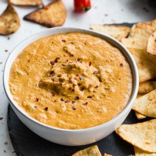 Up close view of cashew queso in a white bowl surrounded by tortilla chips.