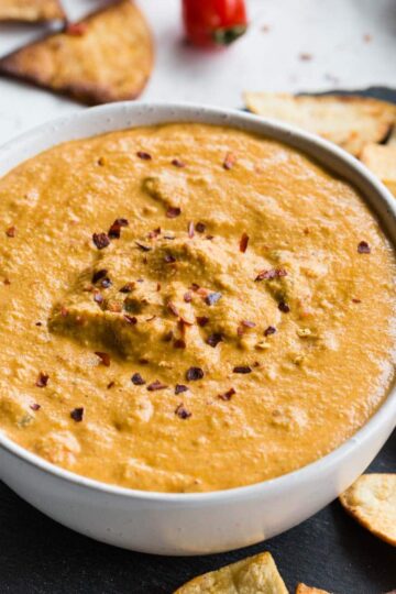 Up close view of cashew queso in a white bowl surrounded by tortilla chips.