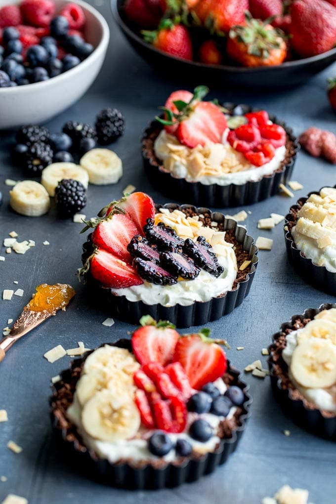Mini fruit tarts arranged on a dark surface next to bowls of berries.