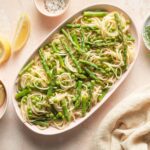 Lemon garlic pasta with peas and asparagus served on an oval plate.