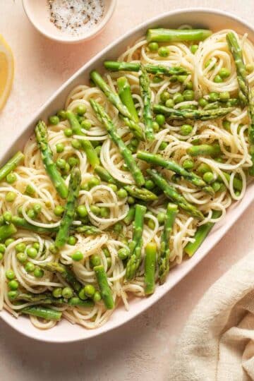 Lemon garlic pasta with peas and asparagus served on an oval plate.