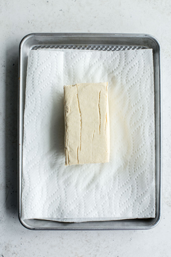 Overhead view of a block of tofu on a paper towel lined baking sheet.