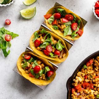 Overhead view of three tacos arranged in a taco stand, with other ingredients surrounding them.