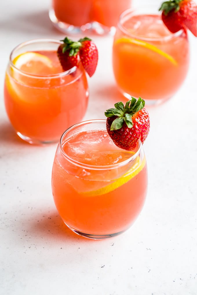 Up-close view of glasses of rhubarb strawberry gin fizz on a light coloured surface.