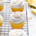 Angled view of vegan pineapple coconut cupcakes on a black wire rack.