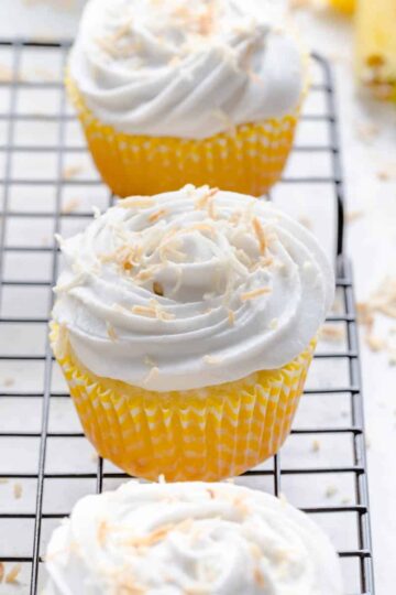 Angled view of vegan pineapple coconut cupcakes on a black wire rack.