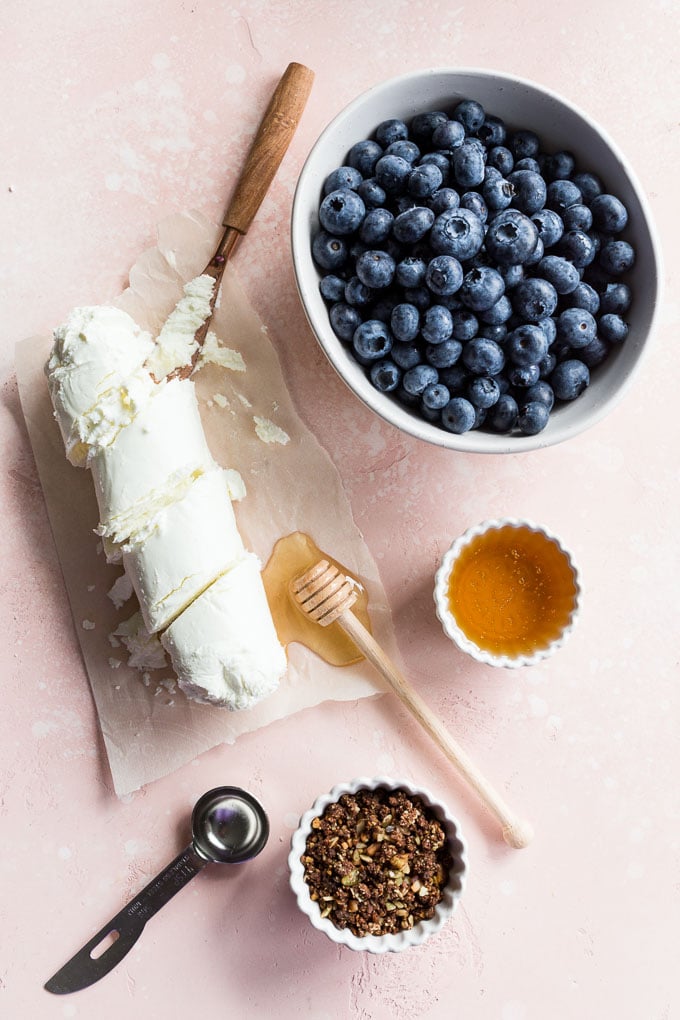 Overhead view of ingredients to make blueberry goat cheese bars arranged on a pink surface.