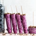 Side view of blueberry goat cheese ice cream bars propped up next to a jar of blueberries.