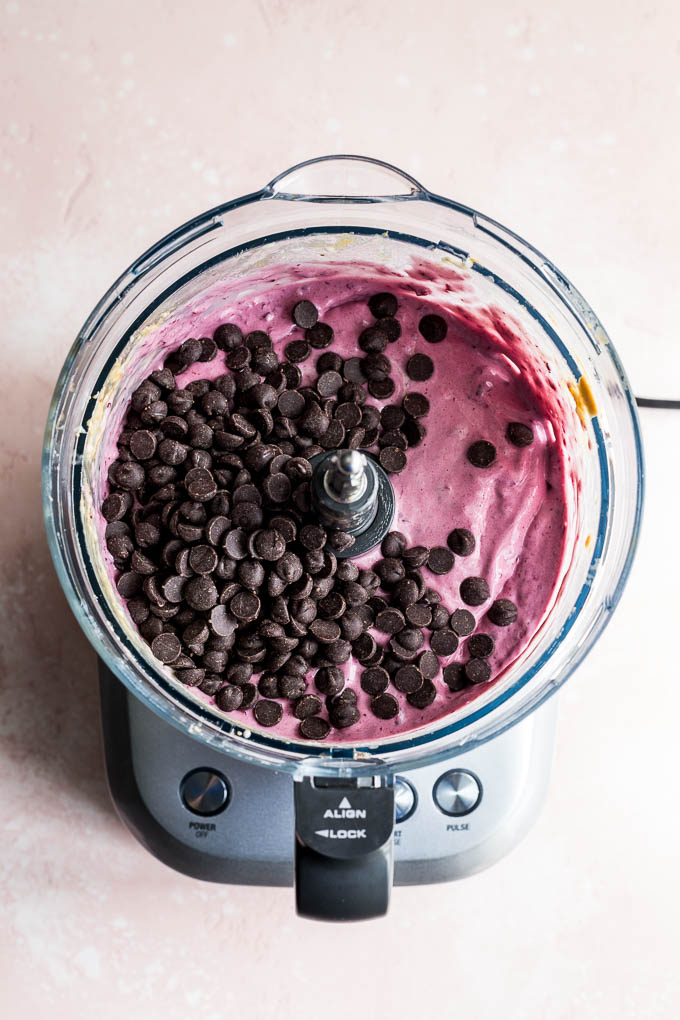 Overhead view of chocolate chips being added to cherry nice cream in a food processor.