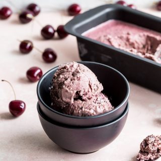 Two scoops of vegan cherry ice cream in a small dark bowl.