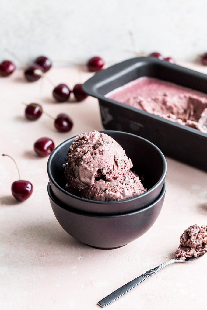 Two scoops of cherry chocolate chip nice cream in a small dark bowl.