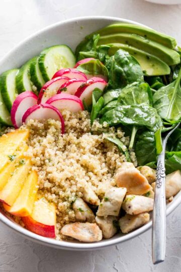 Overhead of chicken peach quinoa salad in a white bowl with a fork.
