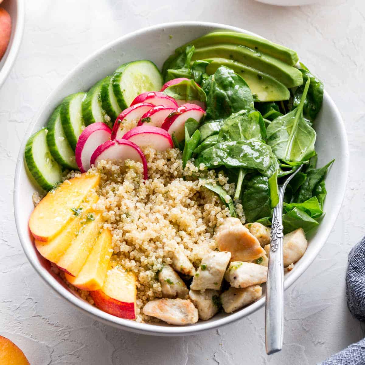Overhead of chicken peach quinoa salad in a white bowl with a fork.