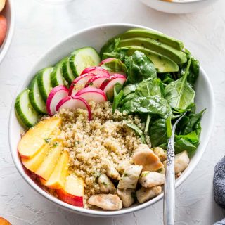 Up-close overhead view of chicken and peach quinoa salad in a white bowl on a white surface.