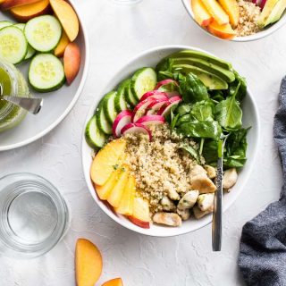 Overhead view of chicken and peach quinoa salad bowls on a white surface.