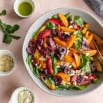 Overhead of stone fruit salad in a grey bowl with vinaigrette and other toppings on the side.