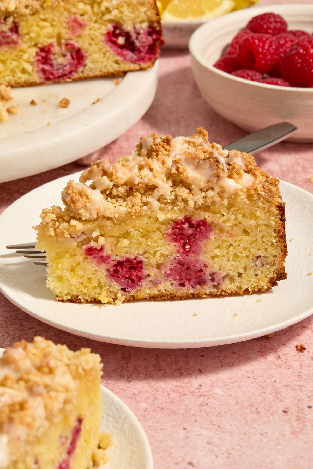Side view of a slice of raspberry lemon cake on a white plate with a fork.