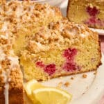 Side view of a slice of almond flour lemon raspberry cake on a white platter.