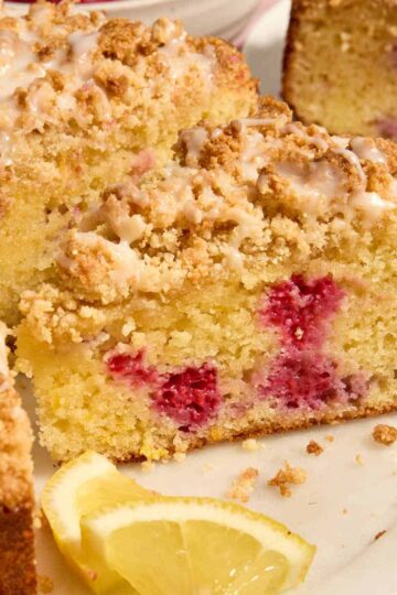 Side view of a slice of almond flour lemon raspberry cake on a white platter.