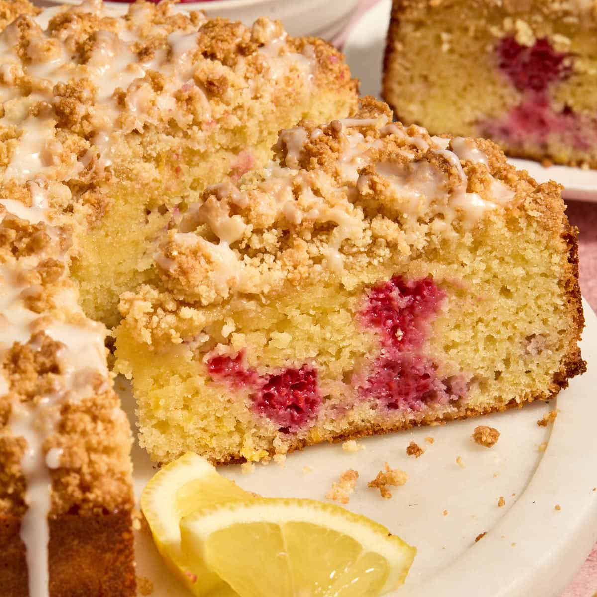 Side view of a slice of almond flour lemon raspberry cake on a white platter.