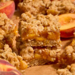 Two almond flour peach crisp bars stacked on top of each other on brown parchment paper.