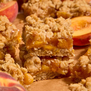 Two almond flour peach crisp bars stacked on top of each other on brown parchment paper.
