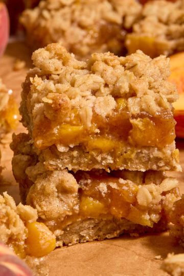 Two almond flour peach crisp bars stacked on top of each other on brown parchment paper.