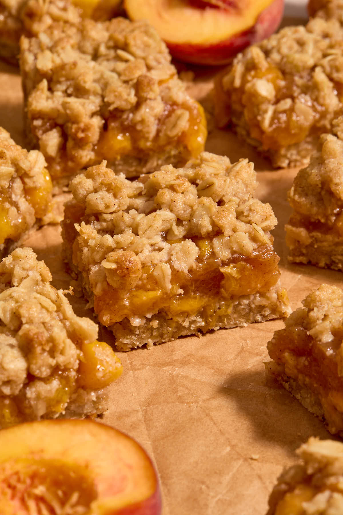 Side view of peach bars arranged on crumpled brown parchment paper with peach halves around them.