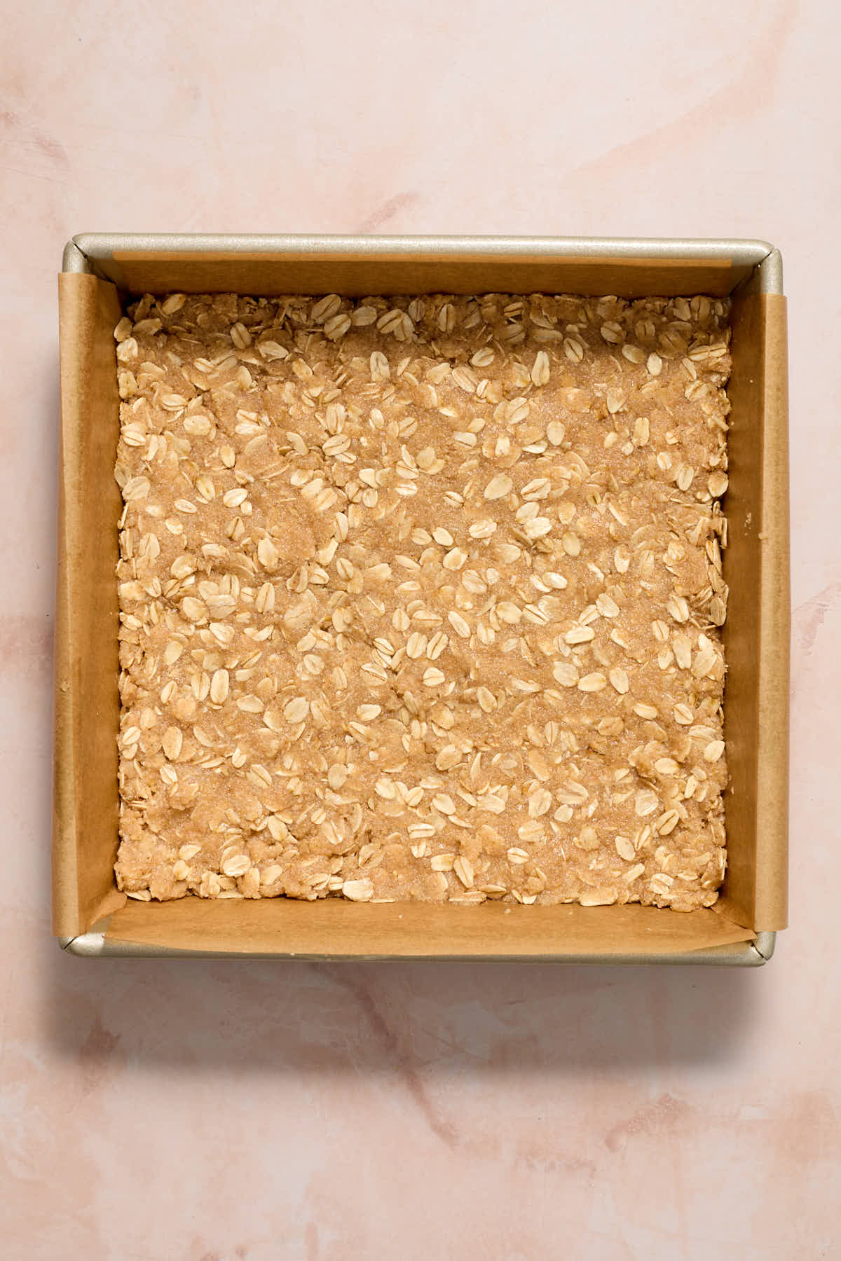 Crust for the peach bars pressed into a parchment lined square pan.