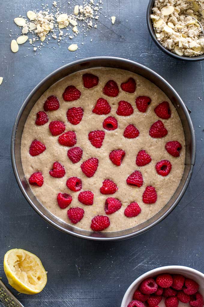 Overhead view of cake batter in a springform pan with raspberries arranged on top.