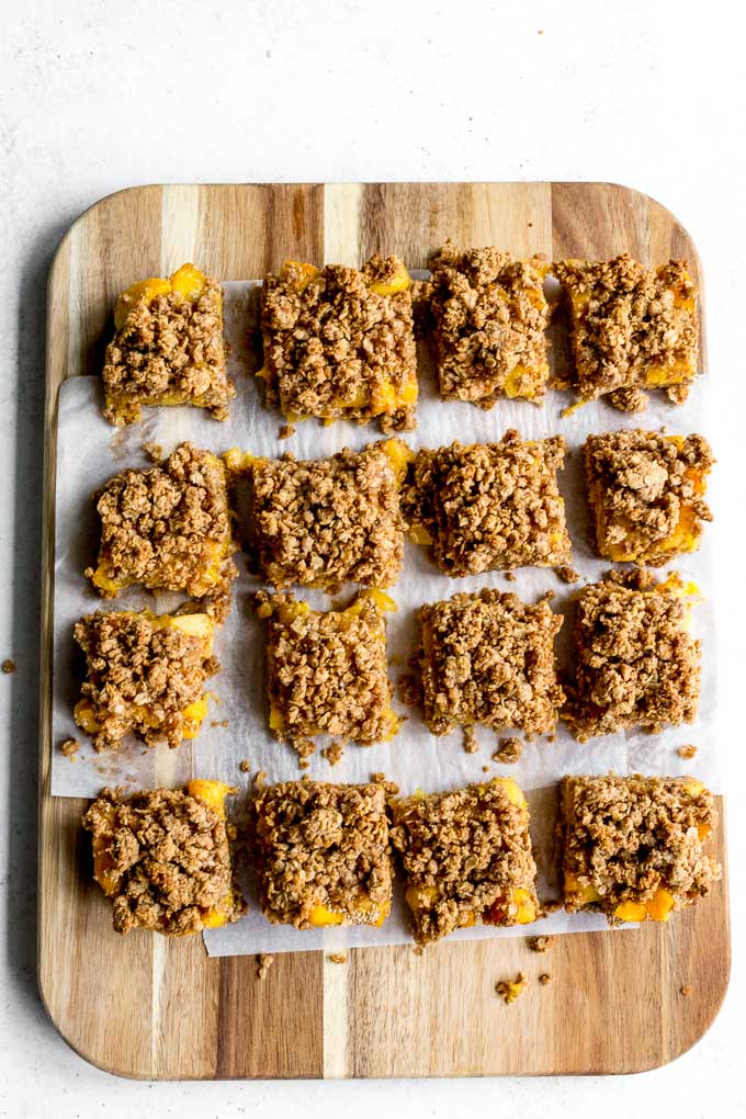 Peach crisp bars cut into squares and arranged on a wooden cutting board.