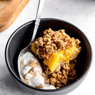 Up-close view of healthy peach crisp bars in a small black bowl with ice cream.