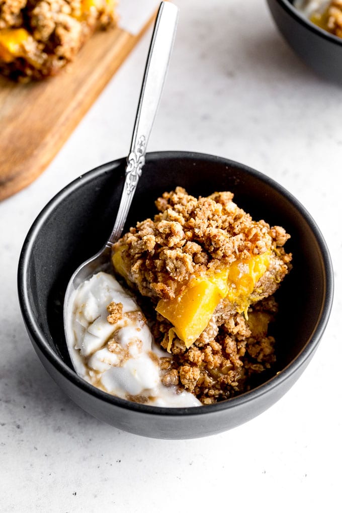 Up-close view of peach crisp bars in a black bowl with ice cream.