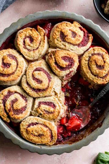 Overhead of strawberry basil cobbler in a pie dish with some removed with a spoon.