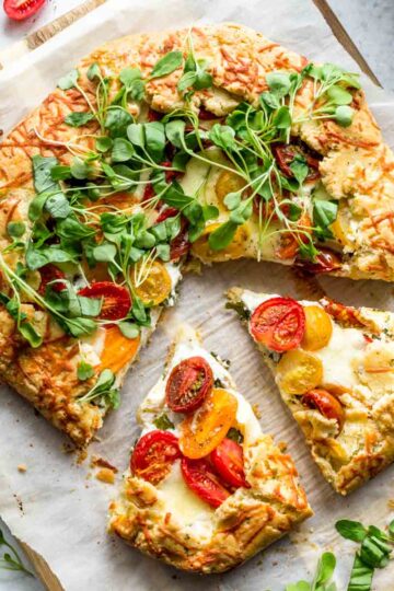 Overhead of a three cheese tomato galette on parchment paper with slices cut out.