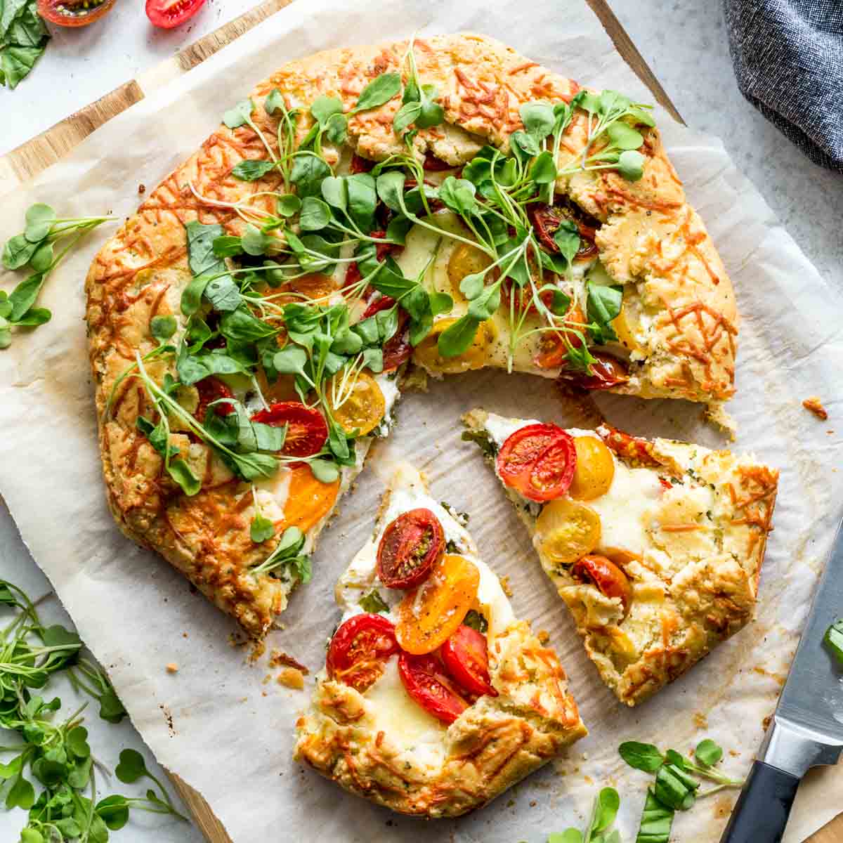 Overhead of a three cheese tomato galette on parchment paper with slices cut out.
