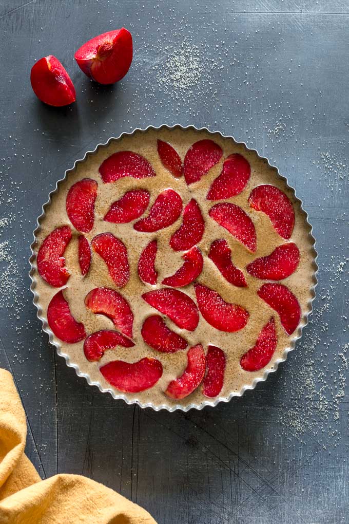 Buttermilk plum cake batter in a round tart pan with plum slices arranged on top.