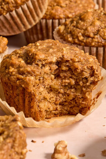Side view of banana nut muffins with one on a parchment liner and a bite removed.