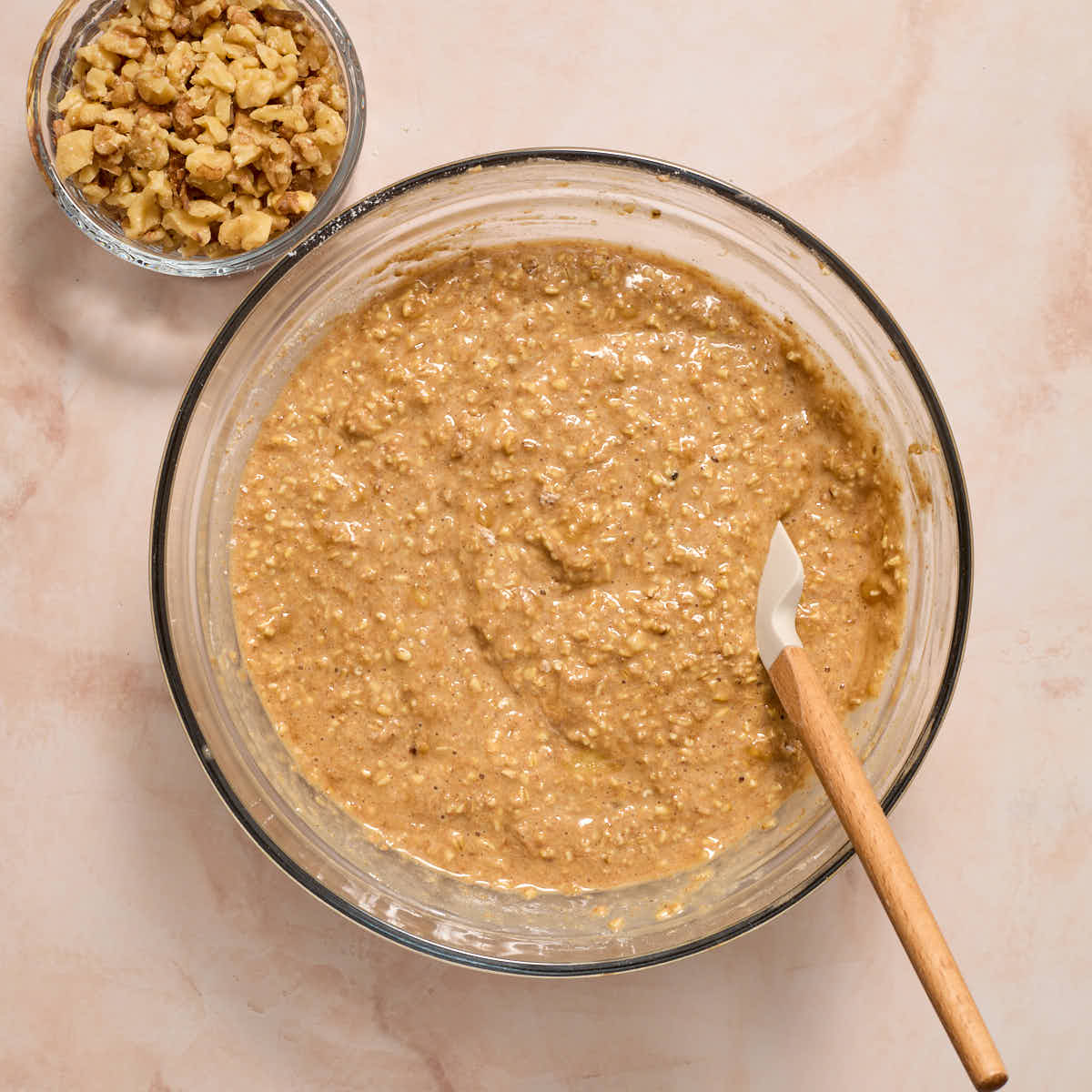 Dry ingredients mixed into wet ingredients with a spatula and chopped walnuts on the side.
