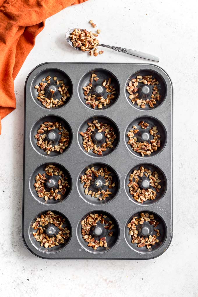 Overhead view of chopped pecans arranged in the cavities of a donut pan.