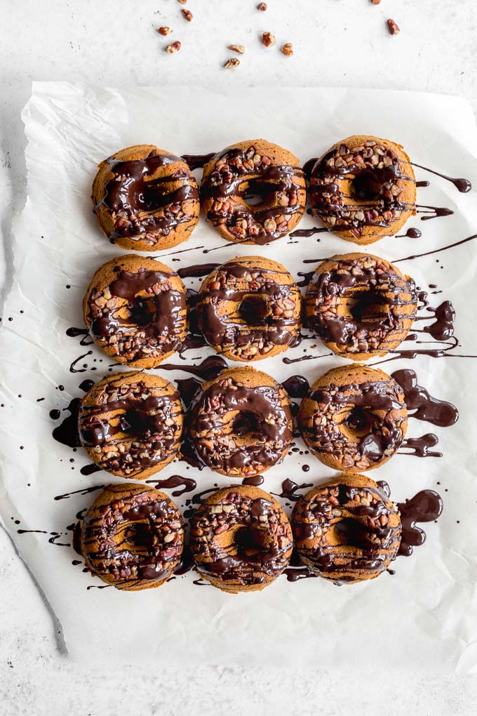 Overhead view of baked pumpkin donuts arranged on parchment paper with melted chocolate drizzled over them.