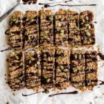 Overhead view of pumpkin spice granola bars on a sheet of parchment paper and topped with melted chocolate and pumpkin seeds.