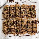 Overhead of pumpkin spice granola bars arranged on white parchment paper with melted chocolate drizzled over them.