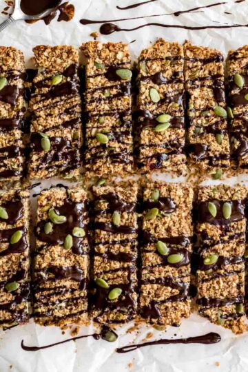 Overhead of pumpkin spice granola bars arranged on white parchment paper with melted chocolate drizzled over them.