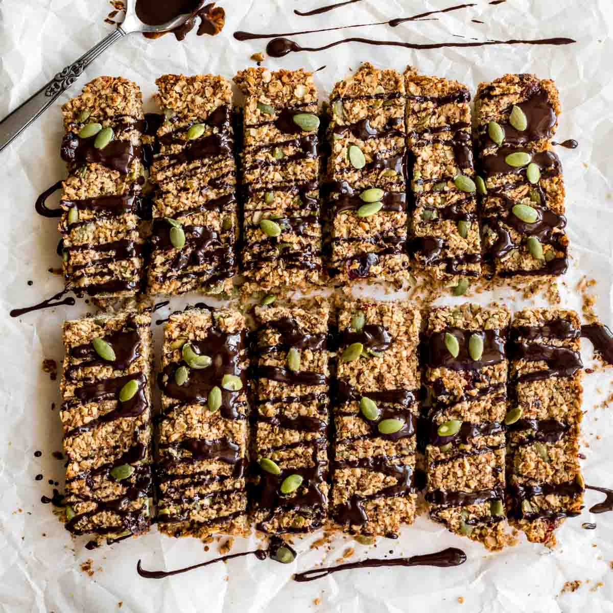 Overhead of pumpkin spice granola bars arranged on white parchment paper with melted chocolate drizzled over them.