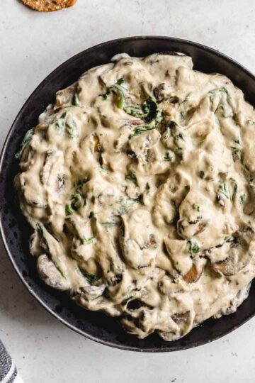 Overhead of creamy cashew mushroom dip in a black bowl with a napkin on the side.
