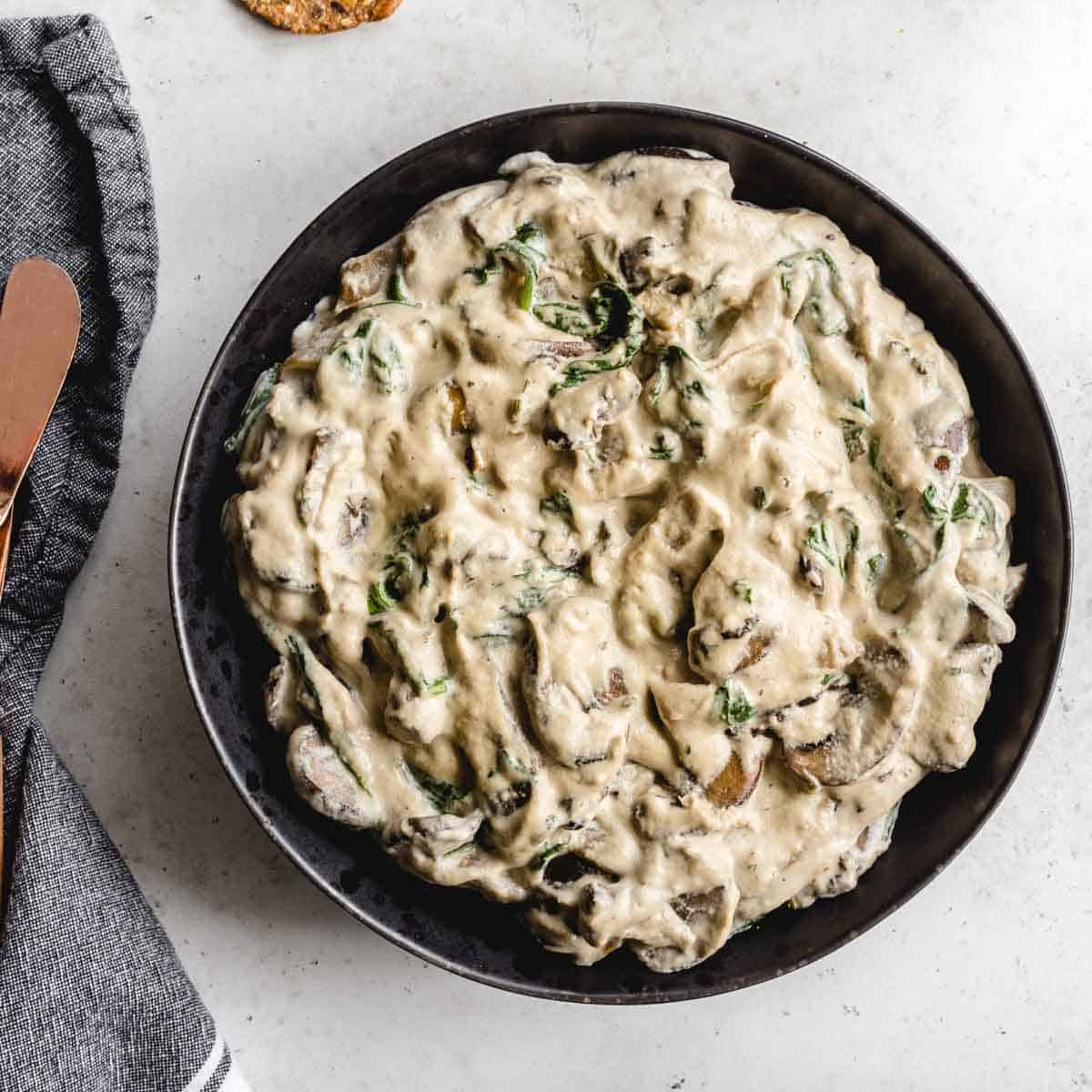 Overhead of creamy cashew mushroom dip in a black bowl with a napkin on the side.