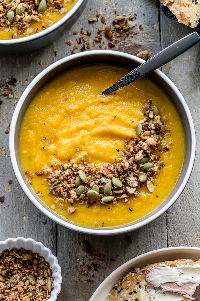Up-close overhead view of golden beet soup in a grey bowl with granola sprinkled on top.