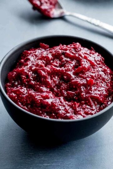 Angled view of healthy cranberry sauce in a small black bowl with a spoon in the background.